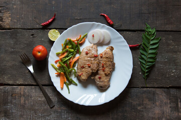 Grilled chicken breast steak slab and vegetable saute in a white plate on a wooden background