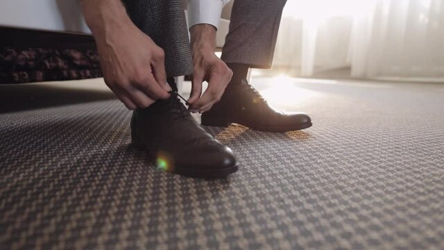 Hands of man adjusting, wearing, putting his wedding shoes in hotel room near window. Groom preparing to go to the bride. Wedding day. Successful businessman bridegroom. Close-up shot. Slow motion