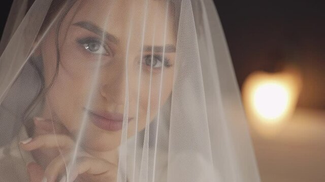 Bride in white boudoir dress under veil and in a silk robe. Wedding morning preparations before ceremony. Luxury bride with fashion hairstyle and makeup. Beautiful, lovely woman in night gown and veil