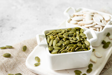Pumpkin seeds in a white bowl on a light gray culinary background closeup