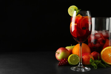 Glass and jug of Red Sangria with fruits on black table, space for text