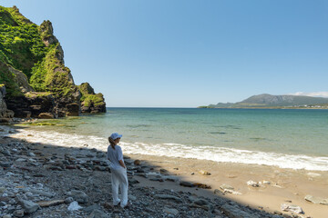 Young woman dressed in white looking at rocky beach at Keel Beach Achill Island Ireland