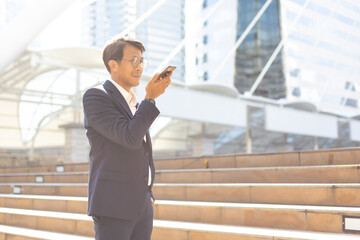 Asian businessman using mobile phone app texting outside the office building