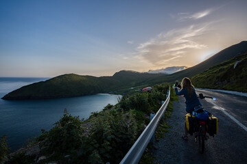 Female traveler cyclist taking a photo of sheep and a panoramic view of Keem Bay in Achill Island...