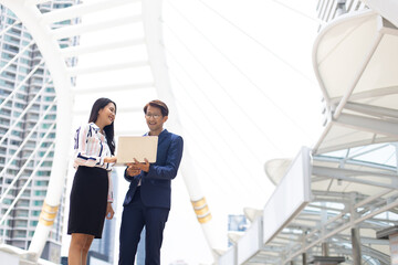 Asian business man and woman working on laptop computer standing outside office building.