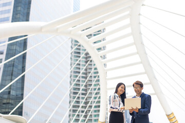 Asian business man and woman working on laptop computer standing outside office building.