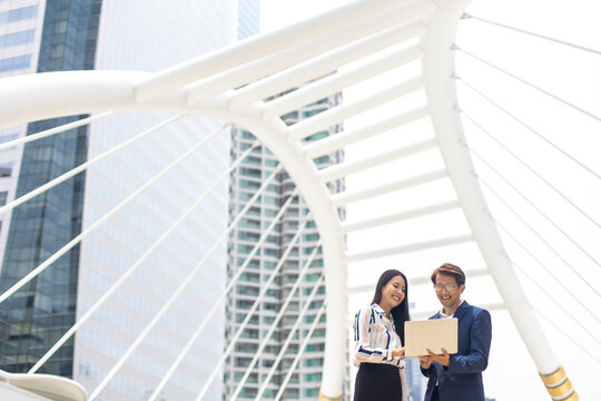 Asian business man and woman working on laptop computer standing outside office building.