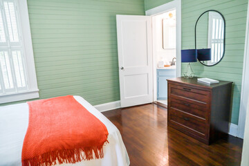 A simple dark wood stained dresser in a guest bedroom with green panel shiplap walls and a black...