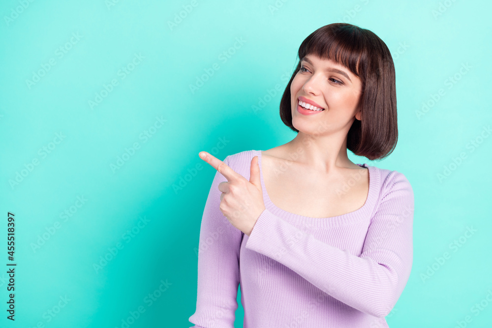 Wall mural Photo portrait woman with bob hair smiling pointing finger copyspace isolated vivid teal color background