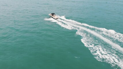 Obraz premium Motorboat sailing in the turquoise sea. Aerial view. Speed boat sailing in the calm sea making foamy waves. Top view during the daytime in Benidorm, Spain. Vacations and travel concept.