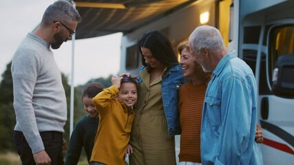 Multi-generation family looking at camera outdoors at dusk, caravan holiday trip.