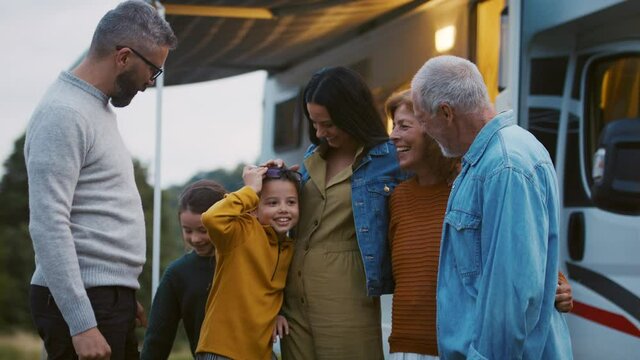 Multi-generation family looking at camera outdoors at dusk, caravan holiday trip.