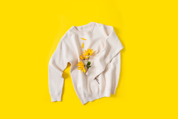 Knitted sweater and autumn flowers on a bright yellow background. Autumn shopping, discount and sale concept. Clothes care, cozy fall. Flat lay, close up. Fall promotion, fashion web line