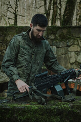 Fototapeta premium Portrait of airsoft player in professional equipment loads a gun with bullets in the forest. Soldier with weapons at war