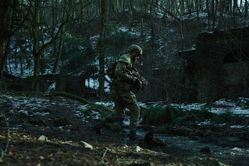 Obraz premium Portrait of airsoft player in professional equipment with machine gun in the forest. Soldier with weapons at war