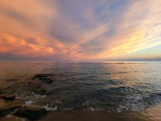 Sunset on the shore of the beach. Multicolored sky, spectacular sunset over the sea with waves on the beach.