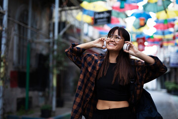 Fototapeta premium Young smiling woman outdoors. Beautiful woman listening to music while walking through the city