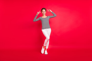 Photo of pretty adorable young woman dressed striped outfit smiling showing two v-signs isolated red color background