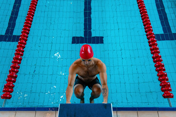 At start. Sportive male swimmer in red cap and goggles in motion and action during training at...