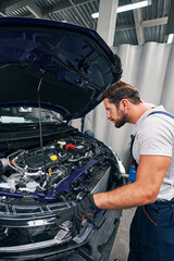 Strong mechanic inspecting car parts under hood