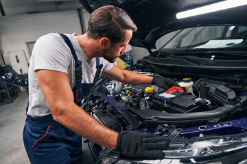Professional mechanic adjusting red battery under car hood