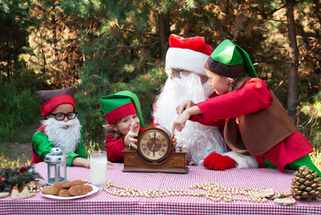 Santa Claus and Helpers Children Elves Sit at the Table for new year and Christmas Reenok pointing...