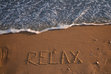 Fototapeta premium Sea wave rolling onto sandy beach with written word Relax, above view