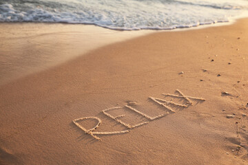 Word Relax written on sandy beach in summer
