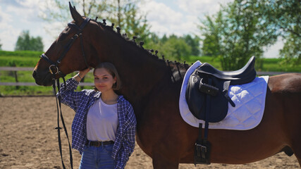 a young girl in an unbuttoned shirt in a white T-shirt stands under a horse's neck and scratches...