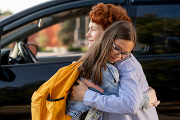 Mother and daughter standing in embrace against car outdoors in the morning