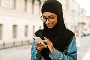 Young muslim woman wearing hijab smiling and using mobile phone