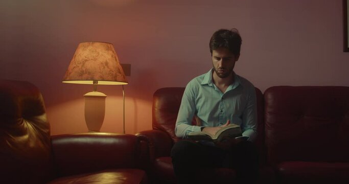 Giovane ragazzo seduto sul divano legge un libro la sera