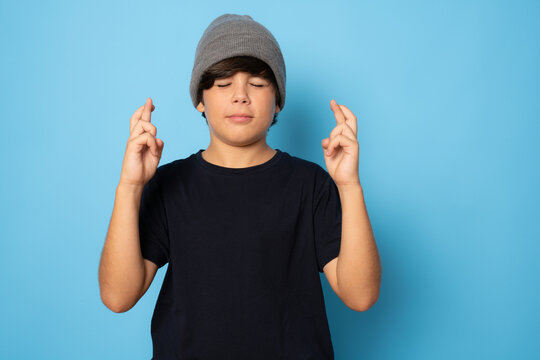 Cute little boy with fingers crossed for luck isolated over blue background.