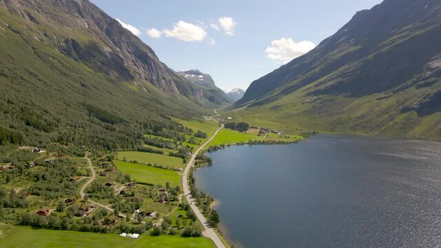 View Of A Small Village And Road At The Foot Of Lush Mountains By The Lake Eidsvatnet Near Geiranger, Norway. - Aerial Drone Shot