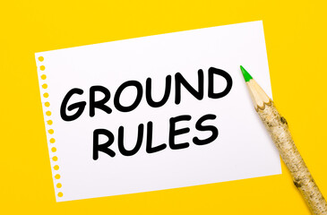 On a bright yellow background, a large wooden pencil and a white sheet of paper with the text GROUND RULES