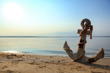 Wooden anchor on river shore near water - obrazy, fototapety, plakaty