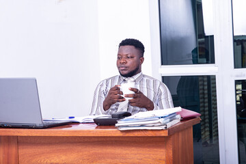 adult businessman holding a cup of coffee and looking at laptop screen in the office.