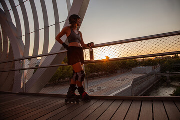 Chica patinadora en línea patinando en un puente de Madrid Rio.  Mujer con accesorios de roller. Chica skate mirando desde un puente el atardecer. Mujer a contraluz. Roller en atardecer. 