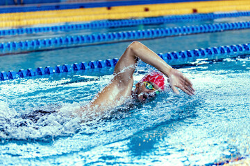 Professional male swimmer in swimming cap and goggles in motion and action during training at pool, indoors. Healthy lifestyle, power, energy, sports movement concept