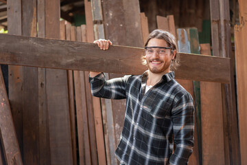 Young male carpenter worker smiling while hold wooden plank at the carpentry workshop