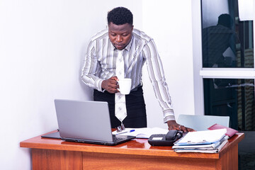 young serious businessman working on the laptop and holding a cup of coffee.