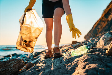 World environment day. An activist picks up a plastic bottle on the beach. Close up. In the background, the sea and the sunset. Bottom view. The concept of cleaning the coastal zone