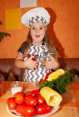 cute little cook in the background of the kitchen for the day of the cook holds two cans of preservation in his hands with emotions of delight opening his mouth Mother's Day preservation
