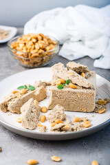 Pieces of sunflower and peanut halva and mint leaves on a plate and a bowl of nuts on the table. Caloric oriental delicacy. Vertical view. Close-up