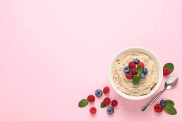 Obraz na płótnie Canvas Tasty oatmeal porridge with raspberries and blueberries in bowl on pink background, flat lay. Space for text