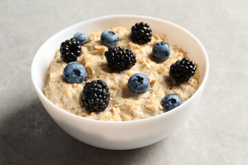 Tasty oatmeal porridge with blackberries and blueberries in bowl on grey table