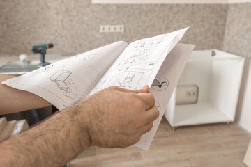 Kitchen installation. Man holds instructions for installing kitchen furniture in his hands