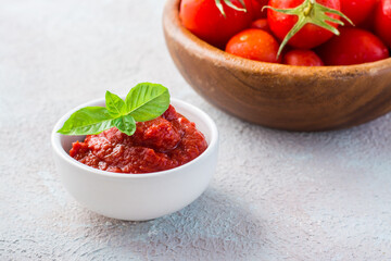 Tomato paste and basil leaves in a bowl and tomatoes on a plate on a light background. Vegetable and vegetarian food. Vitamins and detox diet