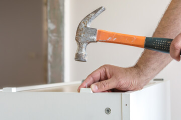 A furniture assembler assembles a kitchen cabinet. Male hand holding an old hammer