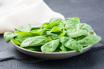 Fresh baby spinach leaves in drops of water on a plate on a slate board on a black background. Vegetarian, wellness and detox food
